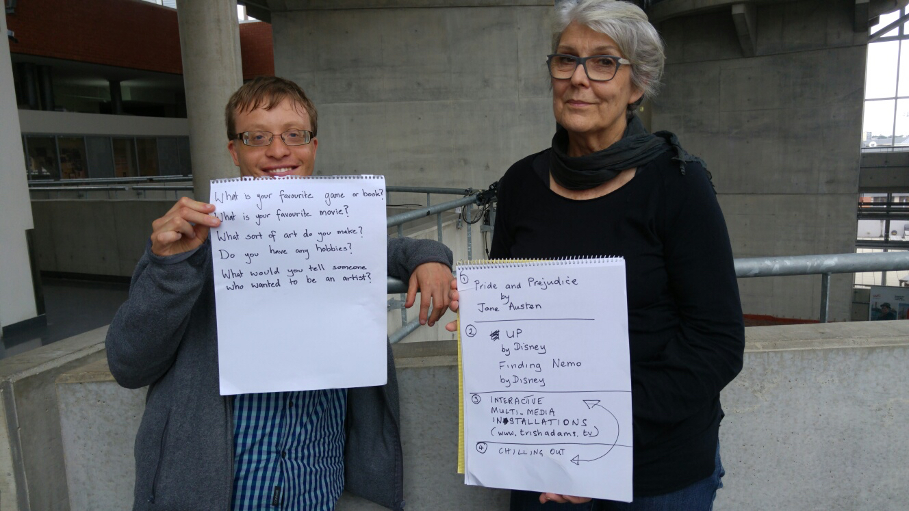 Photograph of James holding a sheet of paper with hand written questions with Trish hold a piece of paper with hand written answers
